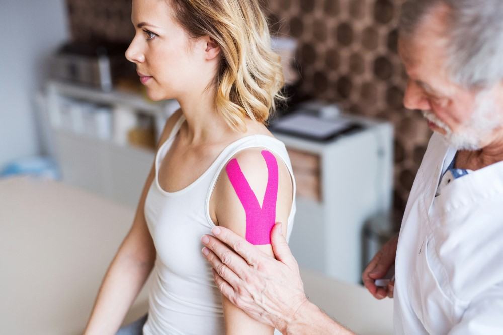 Présentation d'une femme souffrant du syndrome de l'épaule gelée ou capsulite rétractile avec pose d'une bande strech récupératrice