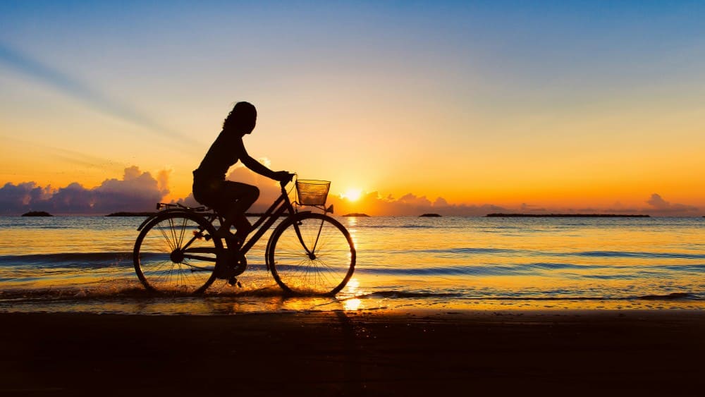 Femme faisant du vélo au coucher du soleil sur une plage