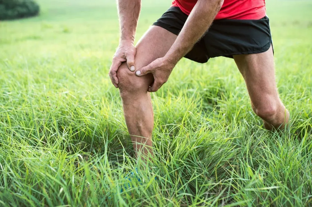Coureur senior de face se tenant le genou en exterieur, sur fond de verdure