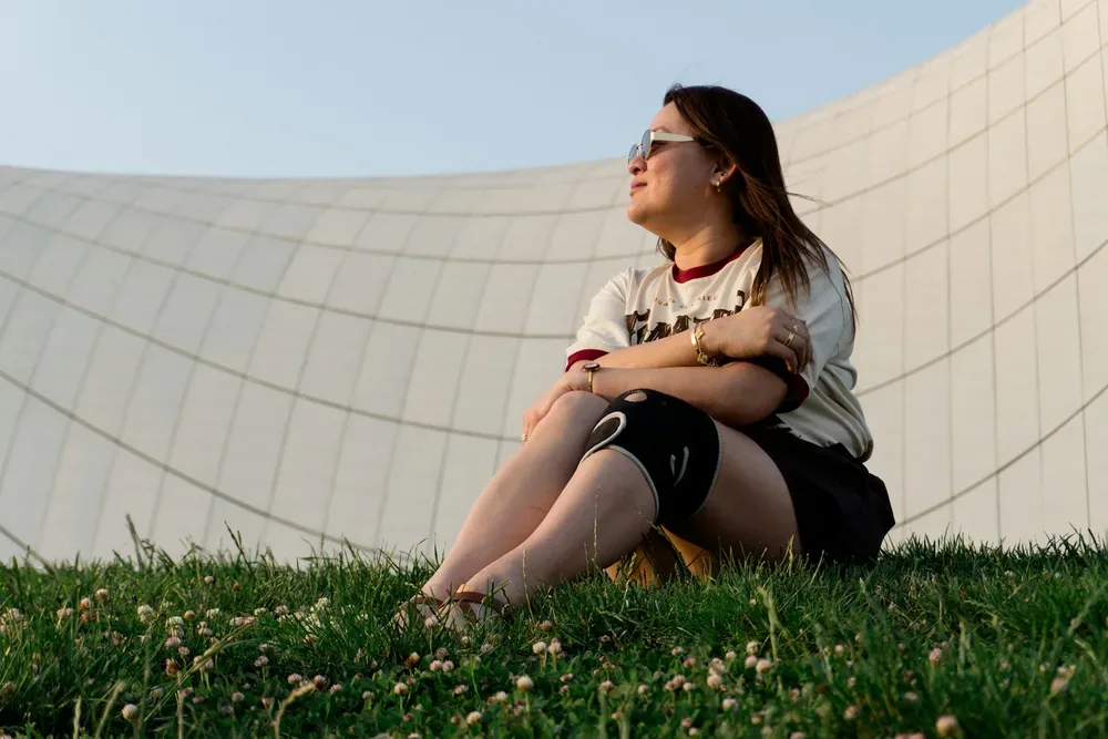 Femme assise sur une herbe verte contre un batiment blanc courbe