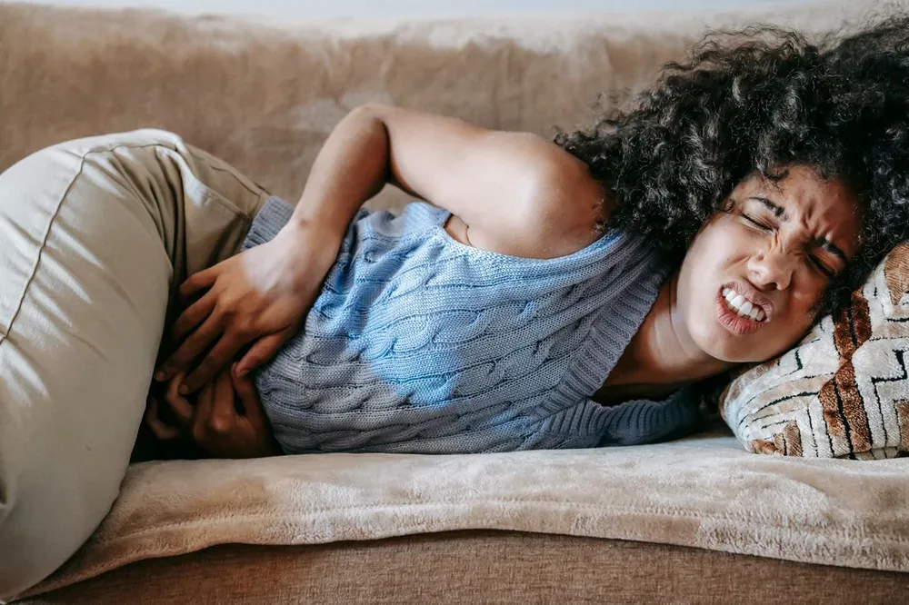 Femme allongée sur un canapé se tenant l’aine et la hanche avec une expression douloureuse.