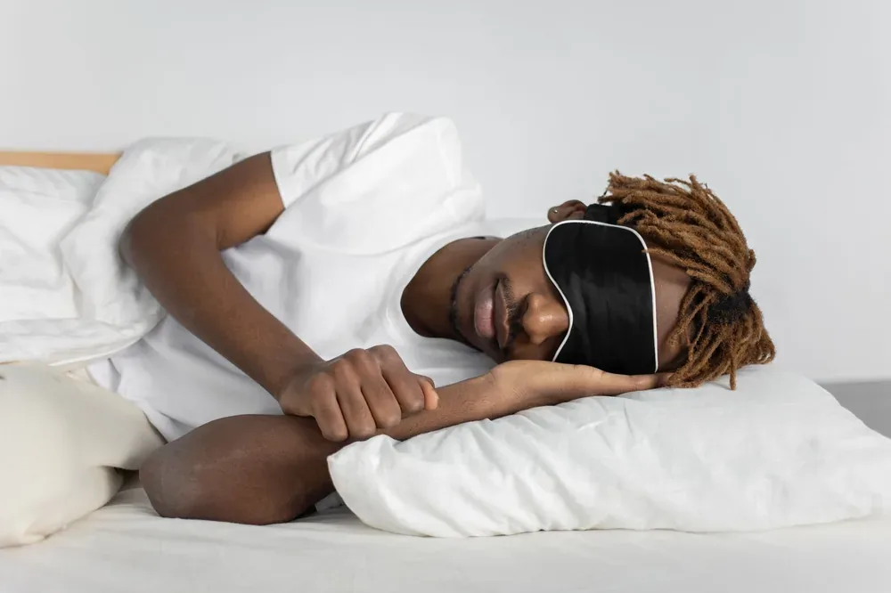 Jeune homme endormi sur le côté avec un masque occultant sur un oreiller