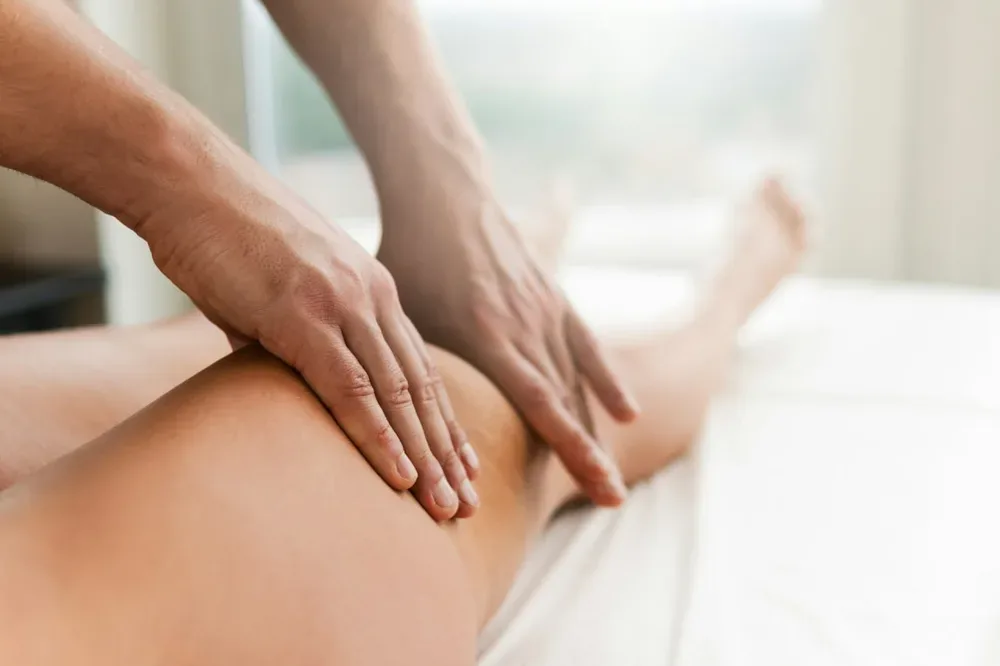 Les mains d'un praticien massent la cuisse près du genou d'une personne allongée.