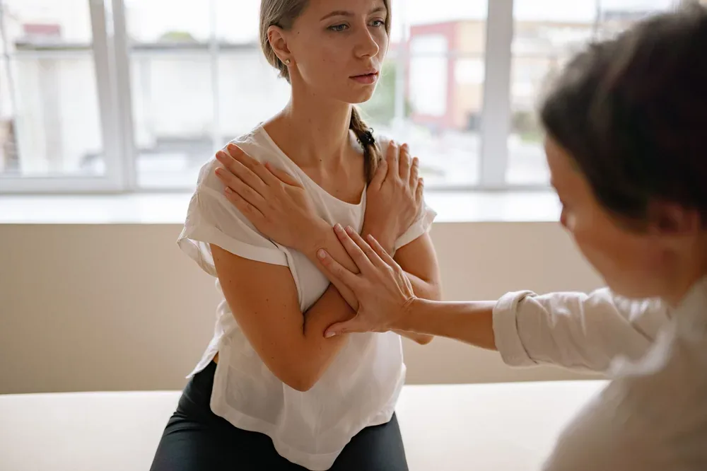 Patiente assise, bras croisés sur la poitrine, examinée par une professionnelle de santé