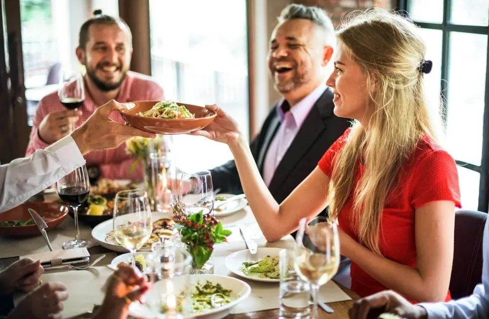Une femme reçoit une assiette lors d'un repas au restaurant, avec des verres de vin sur la table.