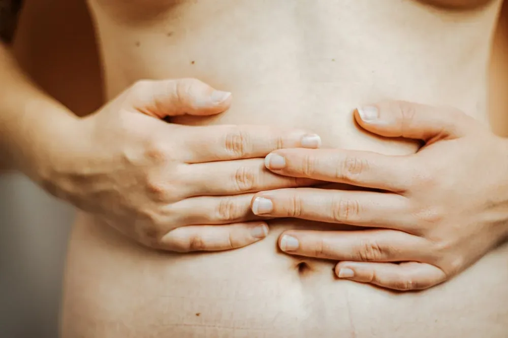 Comment perdre du ventre : une femme pose les mains sur son abdomen pour observer sa silhouette.