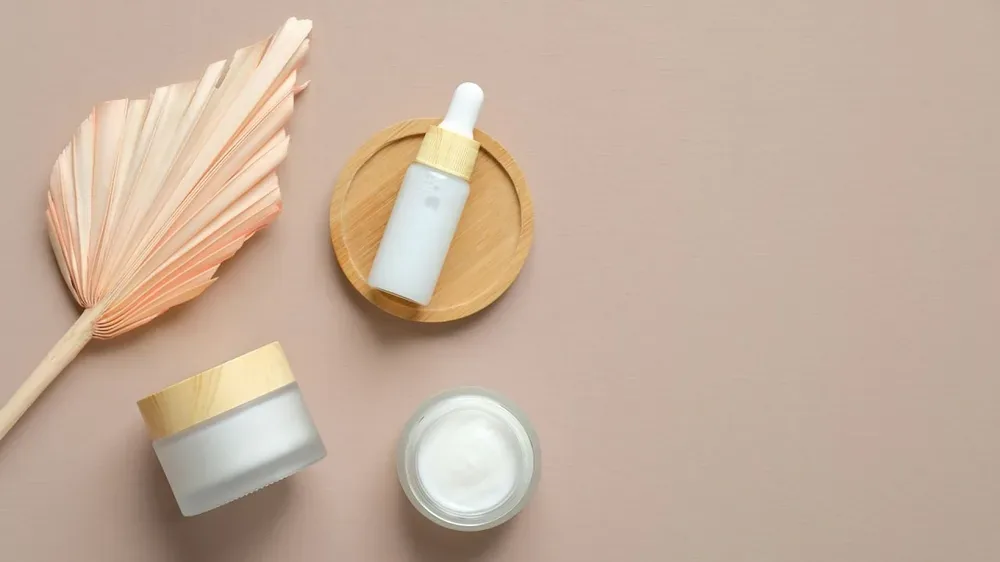 Ensemble de cosmétiques et fleur sèche sur fond beige pour évoquer la simplification d'une routine, sans identifier le contenu des flacons.