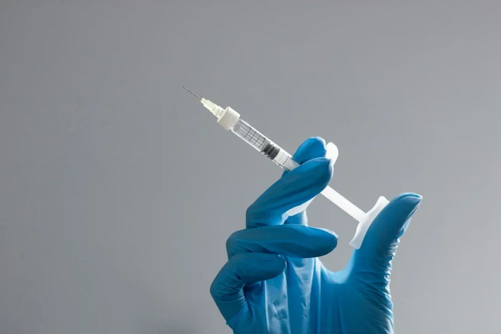 Une main gantée tient une seringue dans un contexte de soin médical